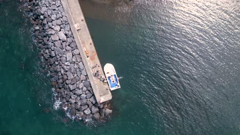 rotating top view of moored fishing boat at the dock jetty with tourists in the summer, azores, porto formoso