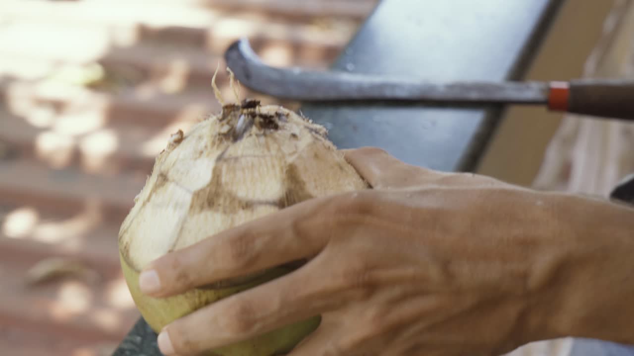 un hombre que sirve un coco abierto con una paja de madera y un machete detrás, barrio de goa, india