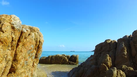 Beautiful-cliffs-on-shore-of-tropical-island-with-yellow-moss-washed-by-calm-clear-water-of-sea,-bright-blue-sky