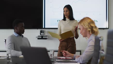 Mixed-race-businesswoman-giving-presentation-to-diverse-group-of-colleagues-in-meeting-room