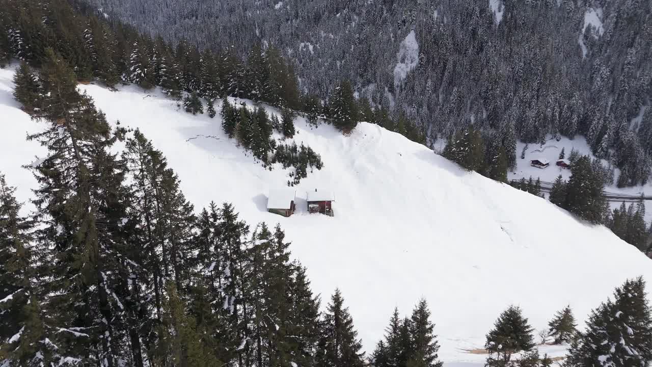 Snow-covered house on snowy hill of alps mountains. Aerial top down shot. Snowy winter day in Switzerland. Conifer trees on slope. Wooden hut for holidays.