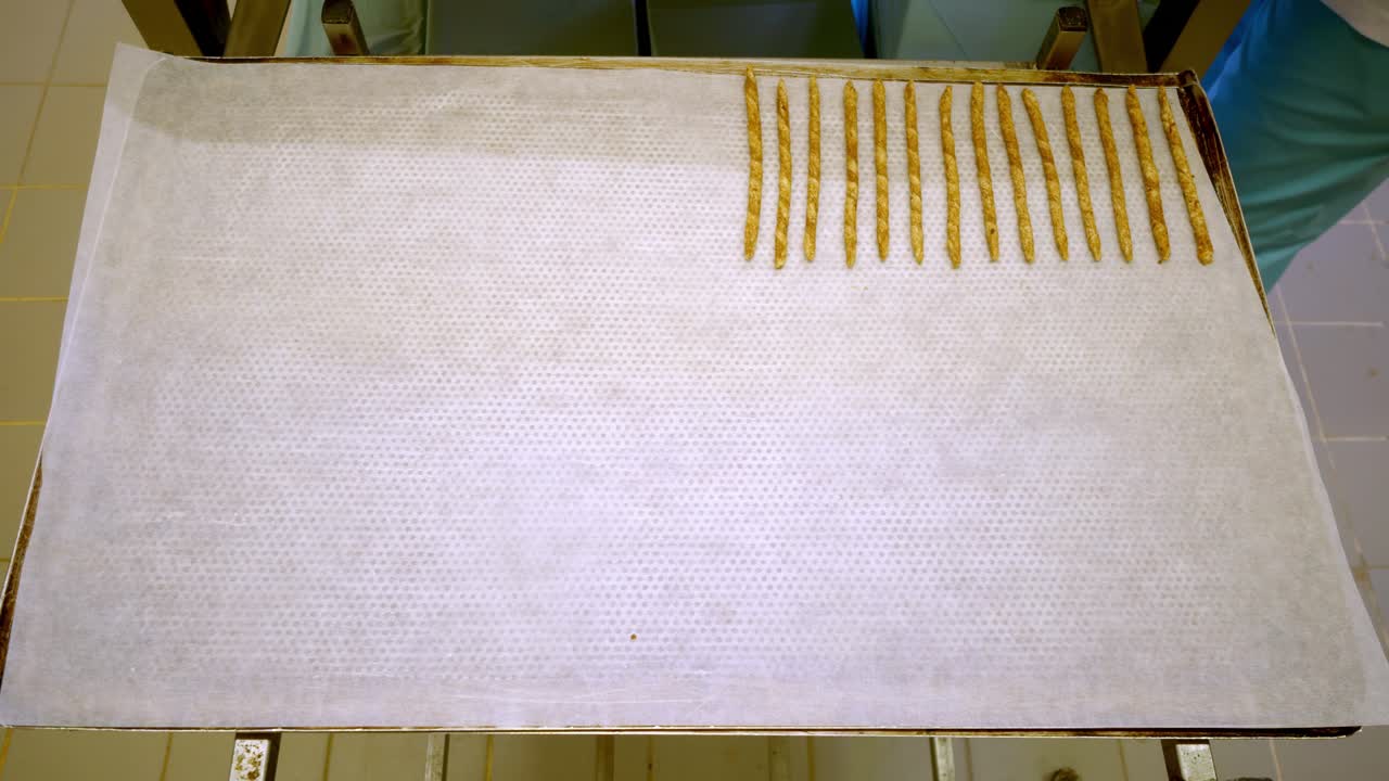 Dough sticks are neatly placed in a row on a baking sheet in an oven tray