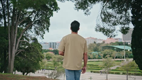 happy tourist walking park alone back view. carefree man looking green garden