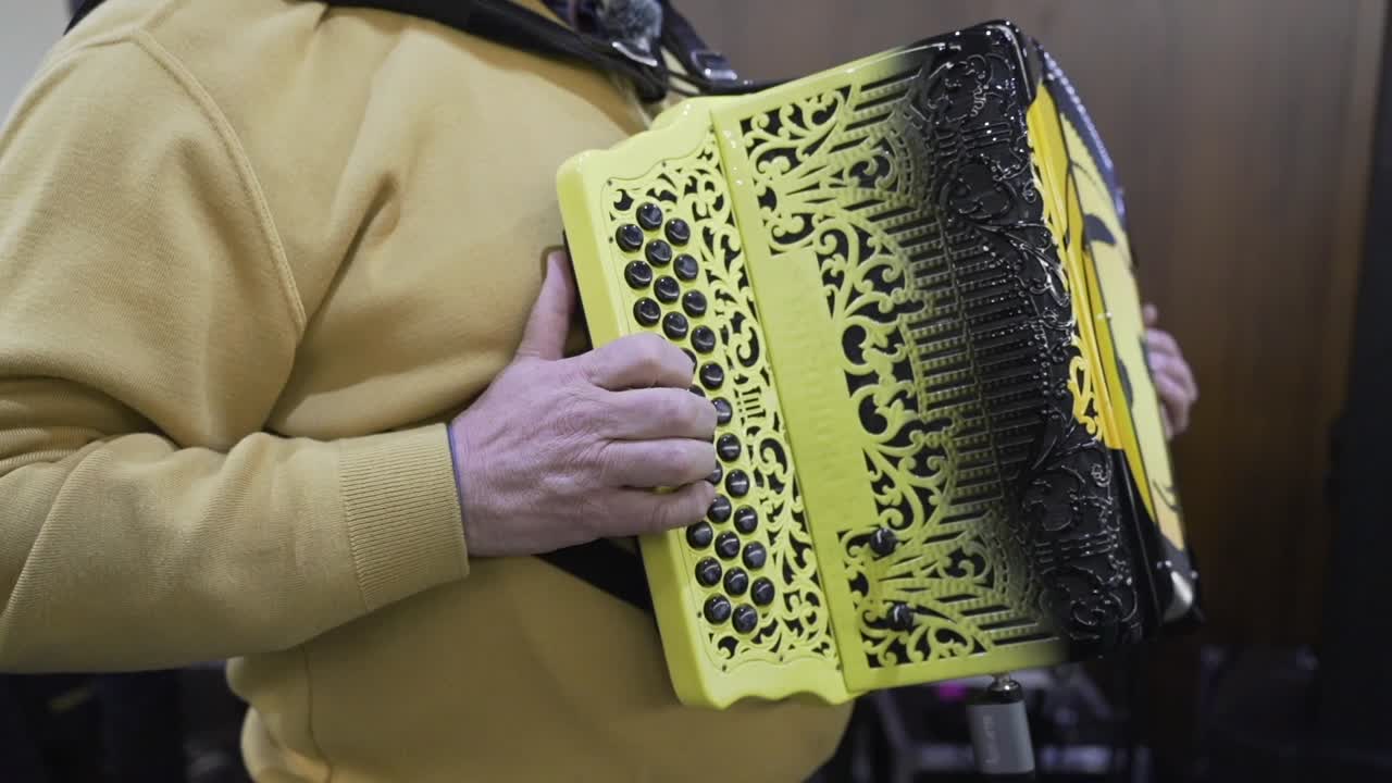Close up of a musician playing a yellow ornate accordion with intricate carvings