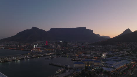 Puerto-Y-Distrito-Urbano-Entretenido-En-El-Paseo-Marítimo-Por-La-Noche.-Adelante-Vuelan-Sobre-La-Costa-Del-Mar-Al-Atardecer.-Ciudad-Del-Cabo,-Sudáfrica