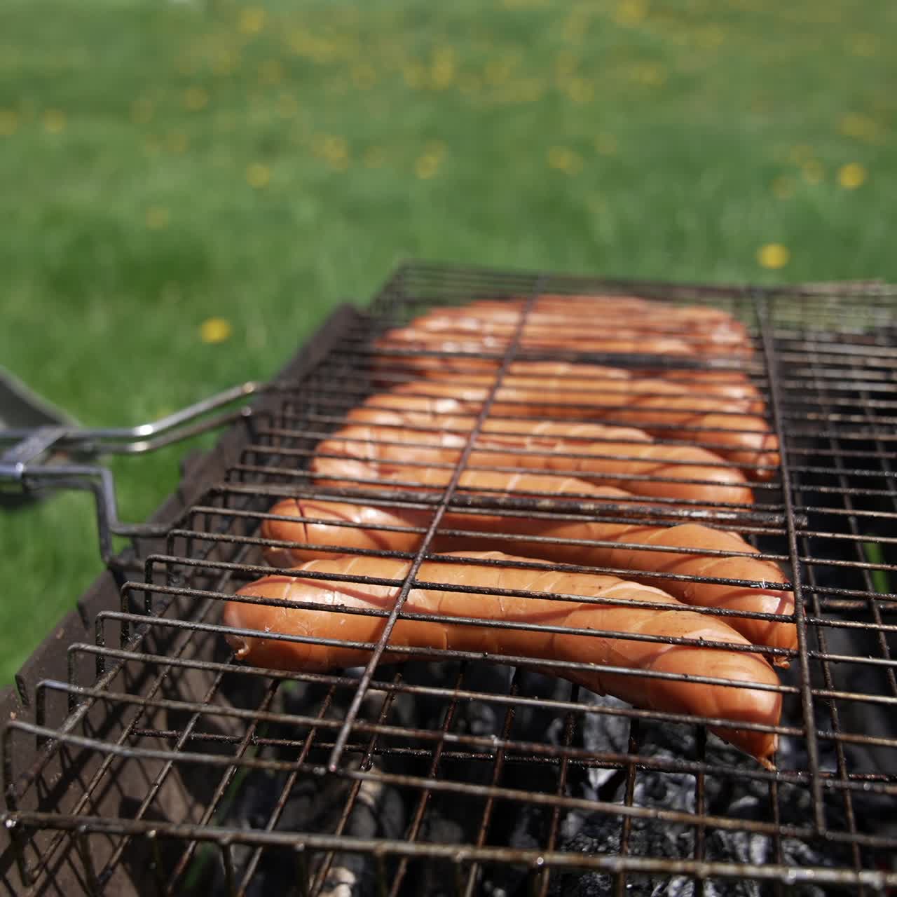 Barbeque sausages grilling for picnic. Man holding on fire roasted meat
