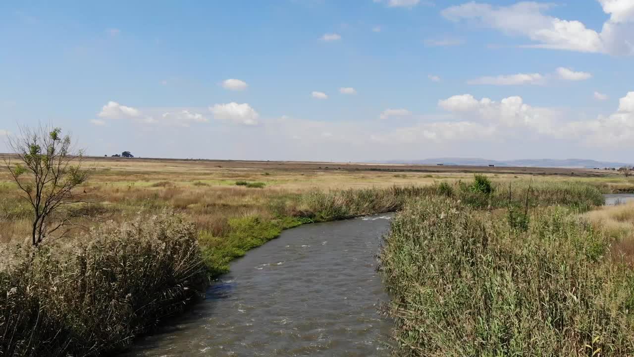 toma aérea de un dron del río que fluye bajo un puente remoto de grava en johannesburgo, sudáfrica