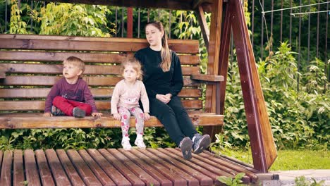 travelling young pretty mother with children swinging on a wooden swing near the summer house 2