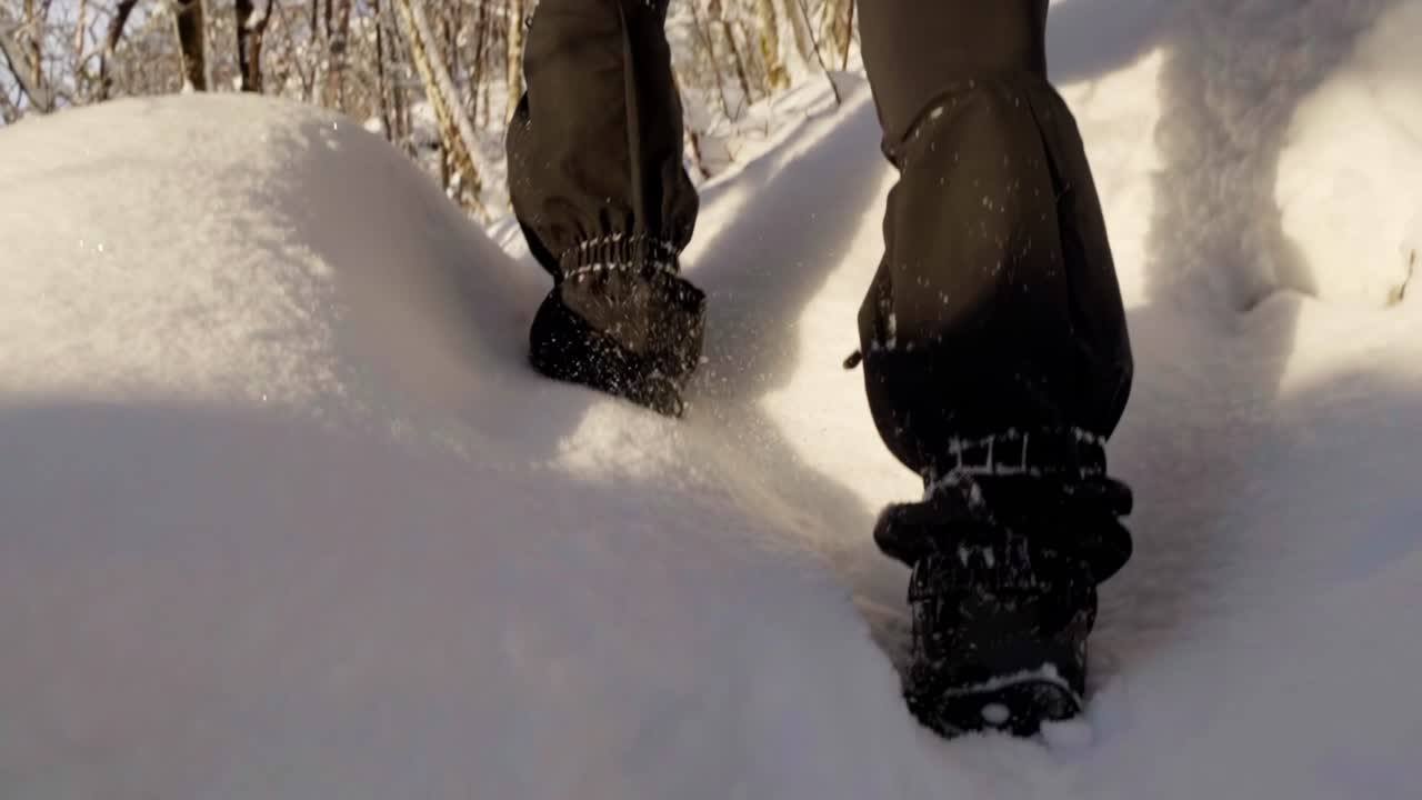 Polainas y crampones, mujer caminando por un bosque nevado, cámara lenta de mano en ángulo bajo.
