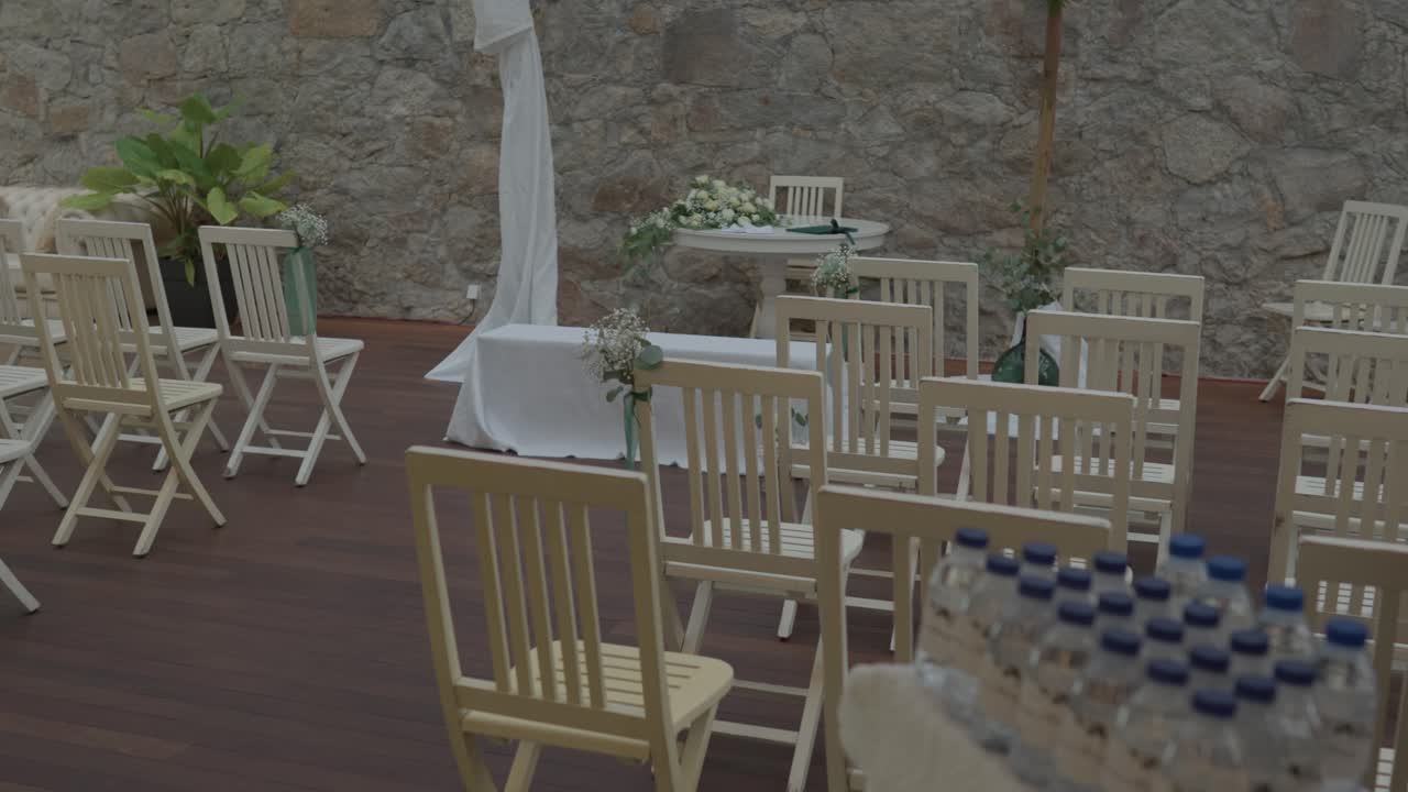 Zona de ceremonia al aire libre con sillas de madera, mesa con tela blanca y decoración floral.