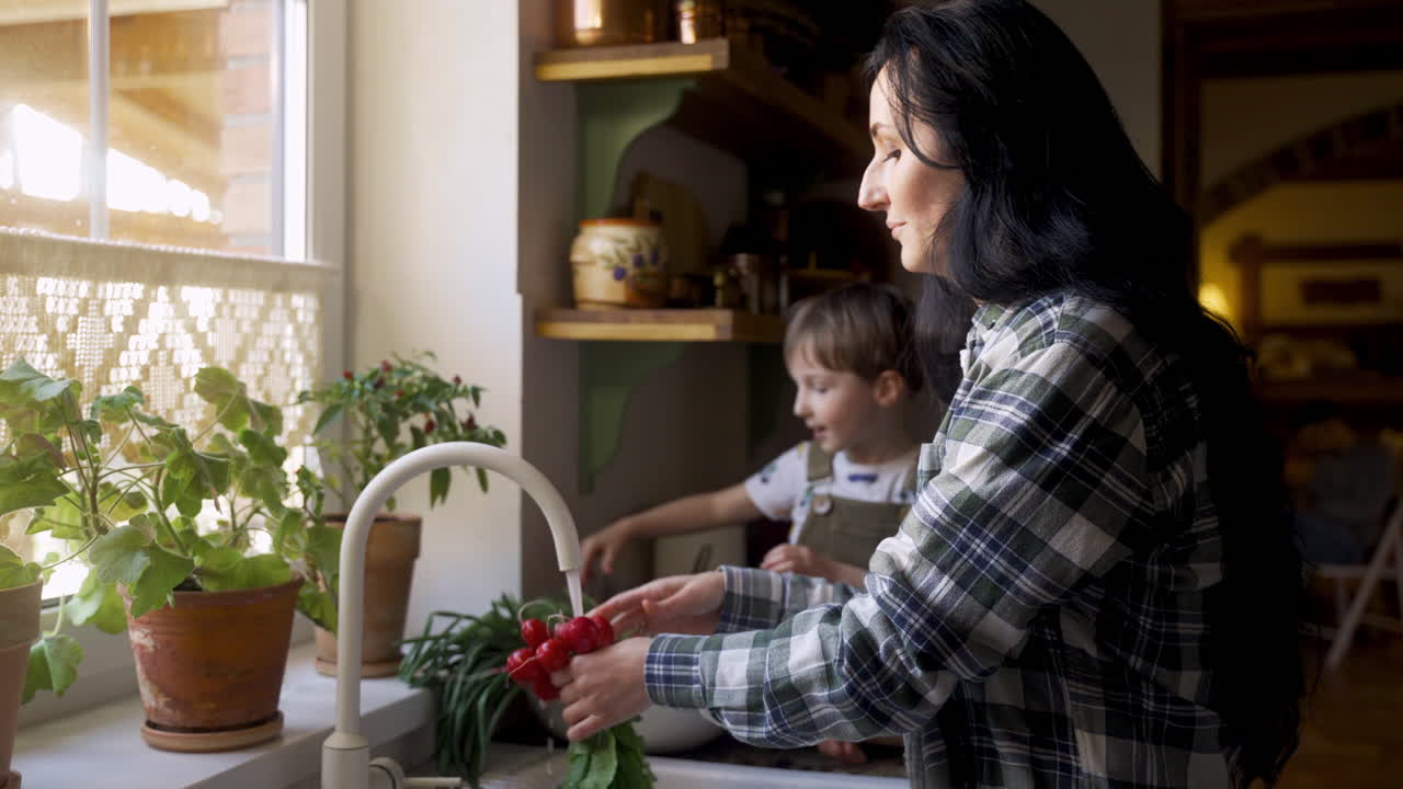 vista lateral de una mujer caucásica lavando verduras y frutas en el fregadero. su hijo la ayuda