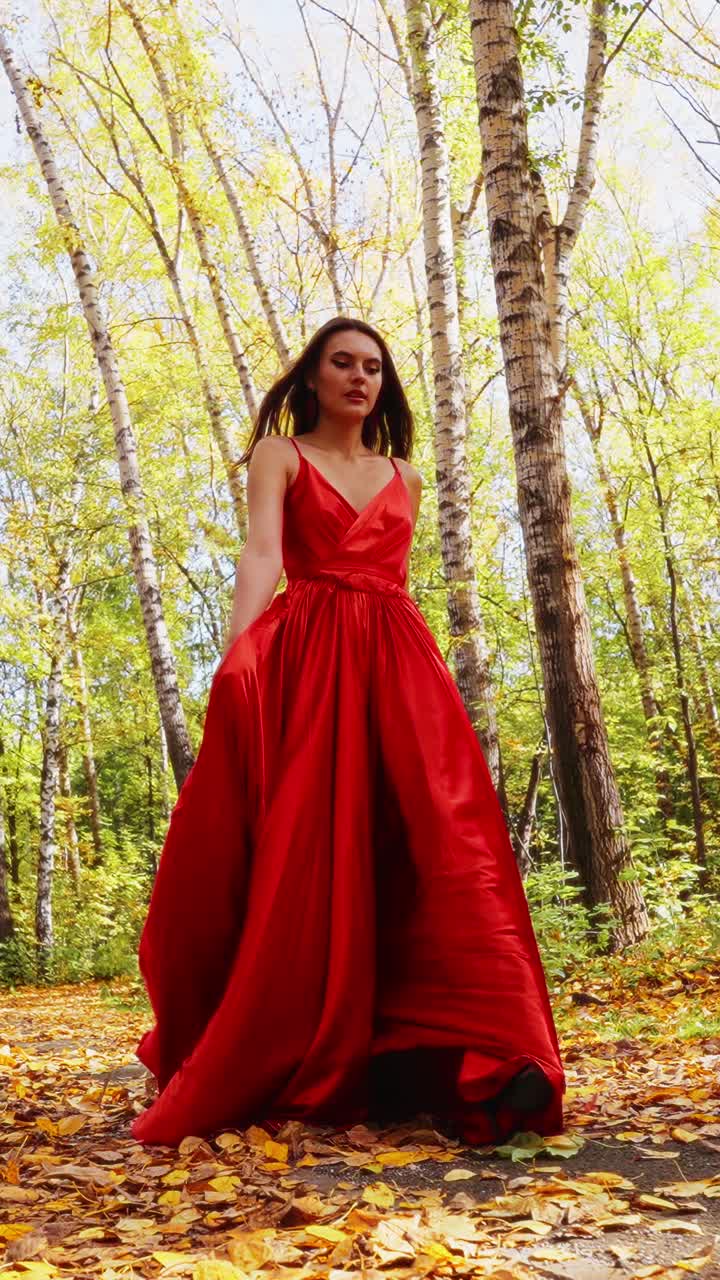 Una figura affascinante in un fluente abito rosso si erge con grazia in mezzo a una vibrante foresta autunnale, catturando l'essenza dell'eleganza e della bellezza della natura in ogni scatto dettagliato.