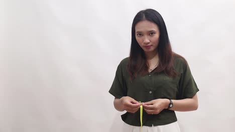 young female in green using a tape measure to measure her waist and pointing at something sideways. isolated on white background