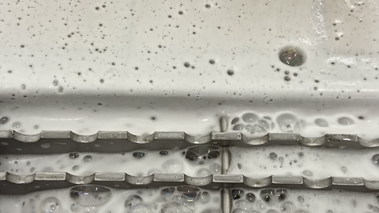 Close-up of white foamy liquid bubbling through stainless steel equipment, milk processing or dairy cleaning operations