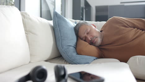 tired senior biracial man lying on couch asleep in sunny living room, copy space, slow motion