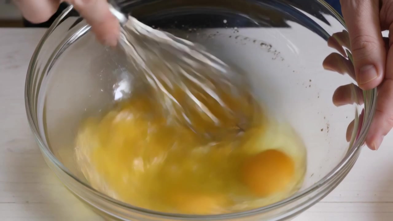 Whisking cook's hands contacting yolks, beating eggs for recipe in bowl on countertop, metal whisk