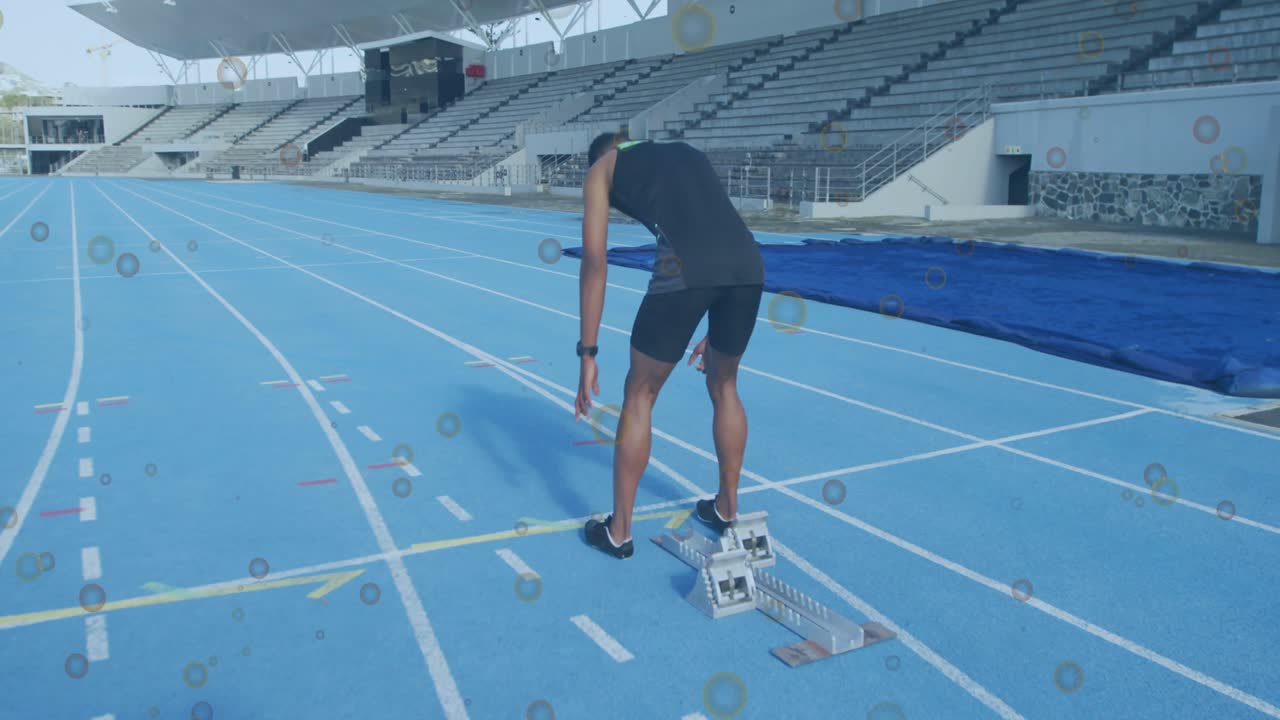 Male athlete shifting weight and stepping into starting blocks on blue track for sprint training