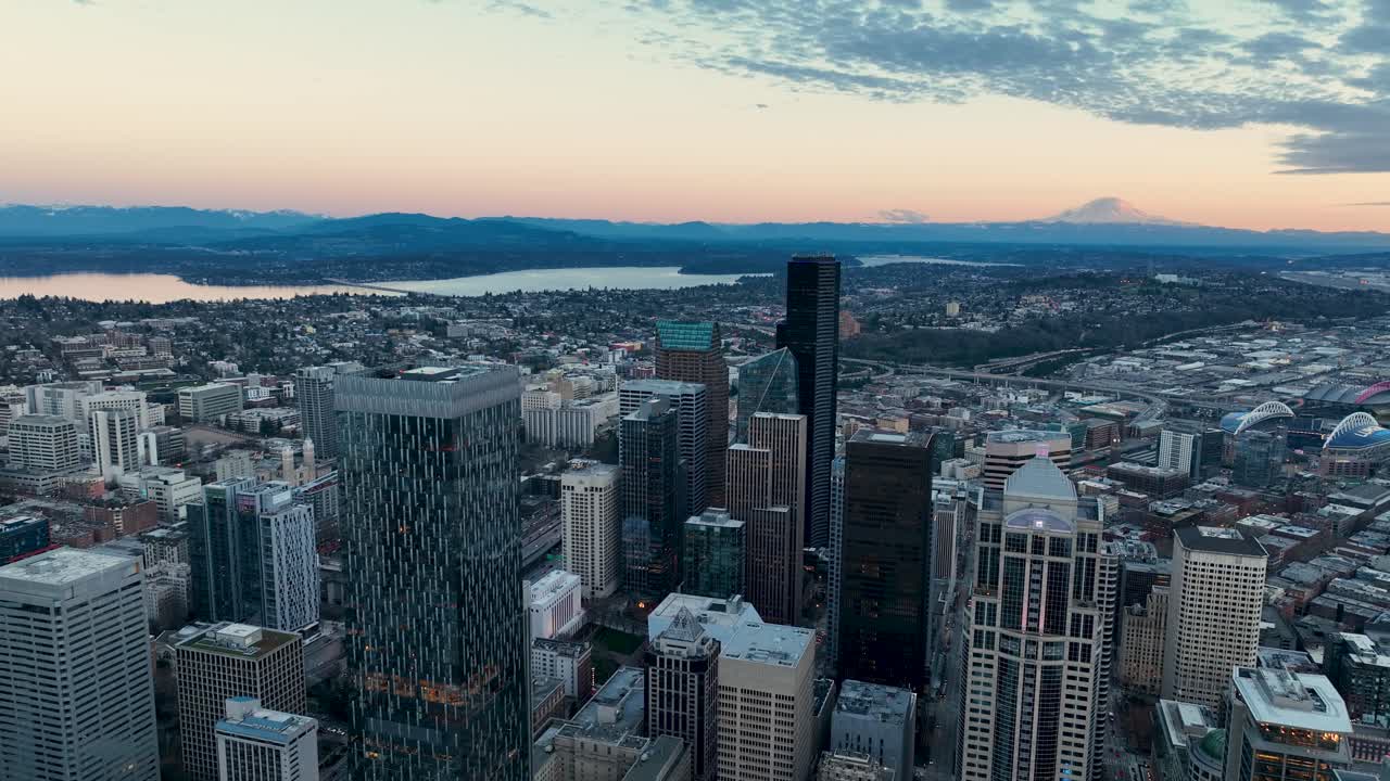 Aerial view of the sun setting behind Seattle's downtown skyscrapers with Mount Rainier off in the distance