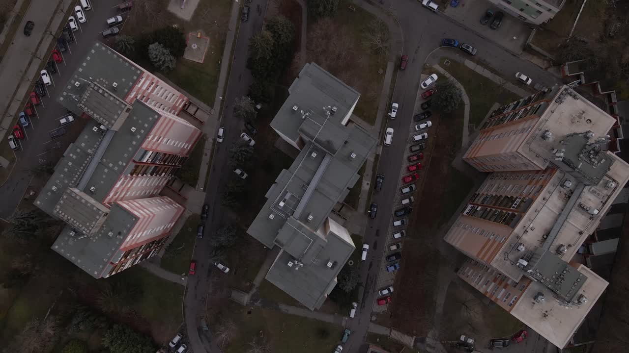 Drone ascent over apartment buildings, surrounded by greenery and roads.