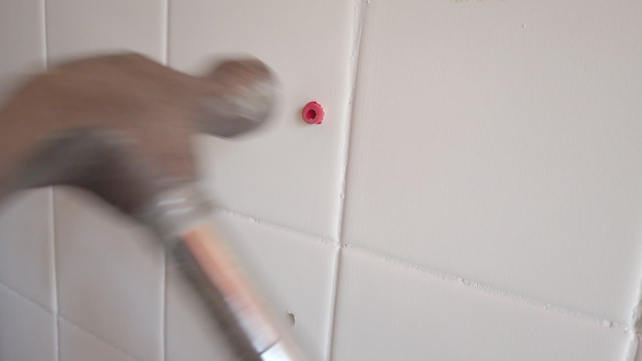 Hammering a Red Wall Plug into a White Tiled Wall