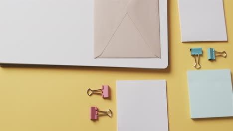 vista aérea de cuadernos, bolígrafos y artículos de papelería dispuestos sobre un fondo amarillo, en cámara lenta