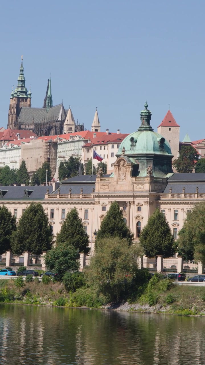 Lenta panoramica orizzontale rivela il Castello di Praga, edifici storici e la riva del fiume sotto la luce del giorno chiara.