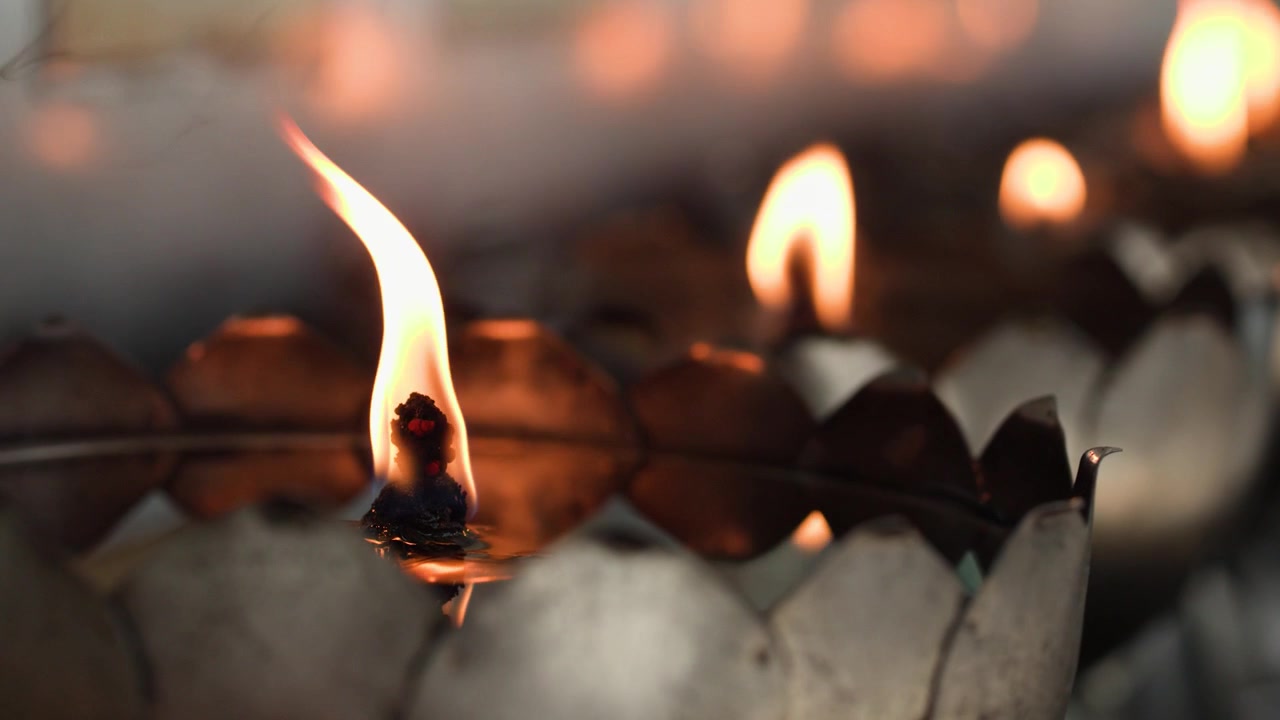 Static close-up shot of flickering orange flames inside decorative metal lotus-shaped oil lamps.
