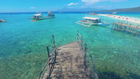 man made bamboo bridge with clear ocean water, boats and sandbar in the backround, sumilon island, cebu, philippines