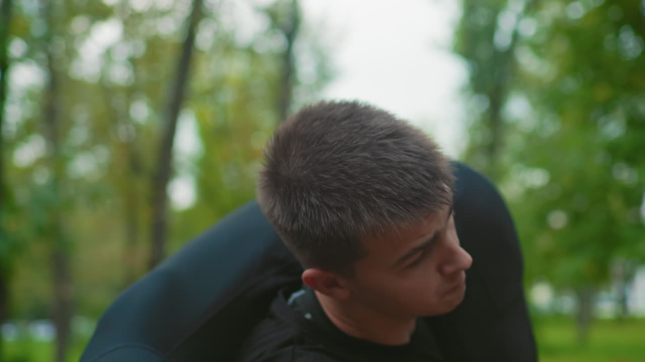 white male trainee collapsing on park path after intense sparring, exhausted boxer with gloves gasping for air, sparring partner pulling hand to assist, coach style encouragement amid autumn trees
