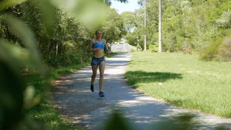 female athlete jogging through green park, perspective through trees, 4k slow motion