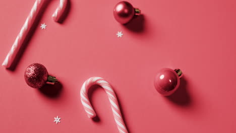 video of baubles and candy canes christmas decorations with copy space on red background