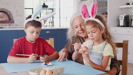 grandmother with grandchildren wearing rabbit ears decorating easter eggs at home together