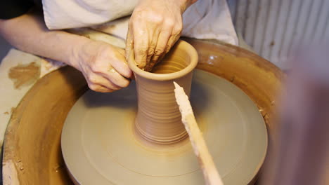 close up of male potter shaping clay for pot on pottery wheel in ceramics studio