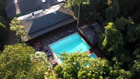 a hotel with a swimming pool surrounded by lush green jungle, aerial view