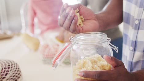 midsection of african american father filling storage jar with pasta, copy space, slow motion