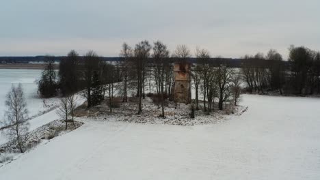 Old-church-bell-tower-ruins-near-snowy-countryside-road-and-agricultural-field