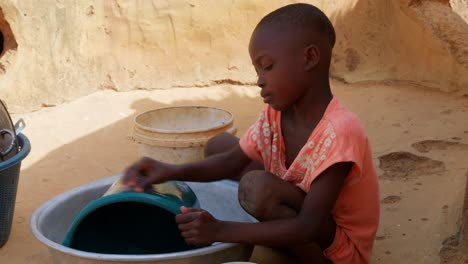 cute little black africa children child washing dishes on a bucket in remote rural village