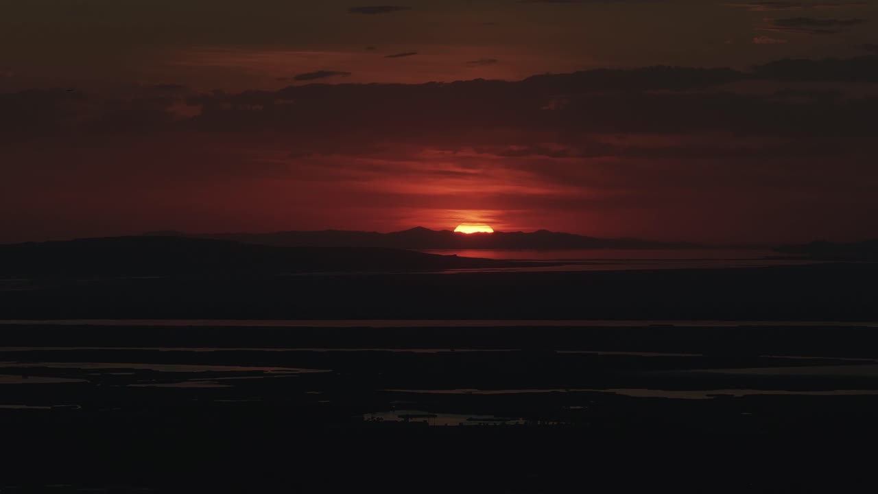 Drone close up shot from Bountiful Canyon in Utah of the sun setting below the Salt Lake Valley with clouds, mountains, and water ponds reflecting light from the Great Salt Lake