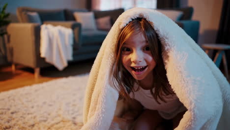 happy child hiding playfully under a cozy blanket in the living room