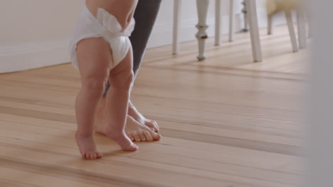 Cerrar-Los-Pies-Del-Bebé-Aprendiendo-A-Caminar.-El-Niño-Pequeño-Da-Los-Primeros-Pasos-Con-Los-Padres-Ayudando-Al-Bebé-A-Enseñar-Al-Niño-En-Casa.