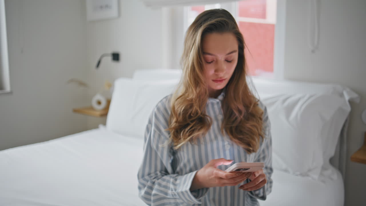 Domestic woman looking smartphone sitting home bed serious face closeup