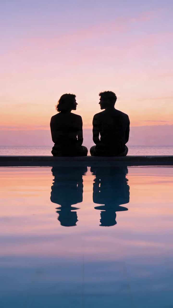 Vertical video: Watching sunset, couple talking in swimwear at infinity pool with sea reflection