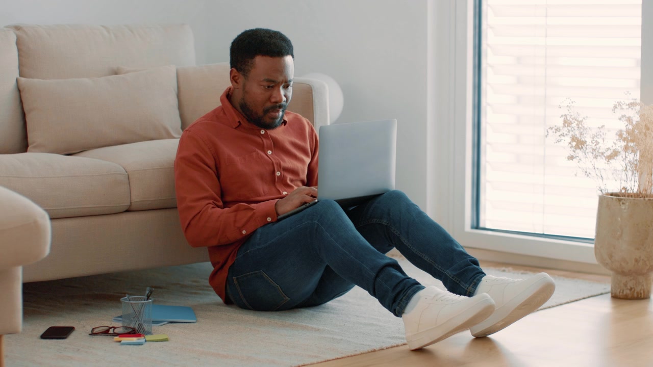 Young Man Working on Laptop While Sitting on Living Room Floor