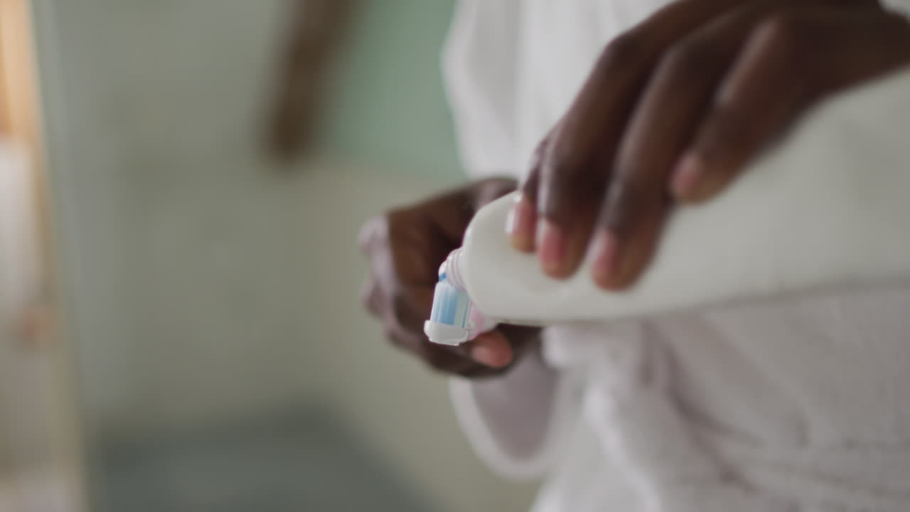Hands of african american attractive woman applying toothpaste on the brush in bathroom