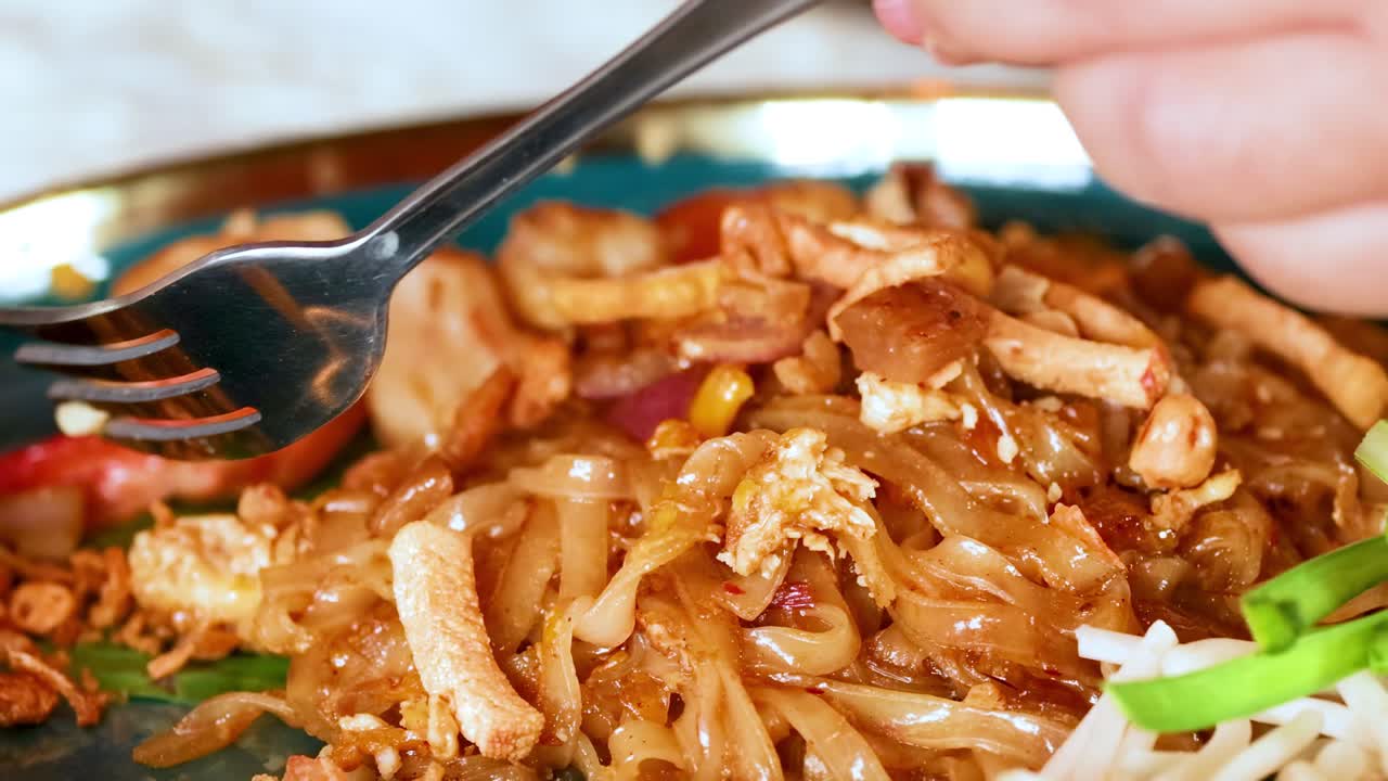 A detailed view of shrimp pad Thai being enjoyed with a fork and spoon, highlighting the vibrant ingredients.