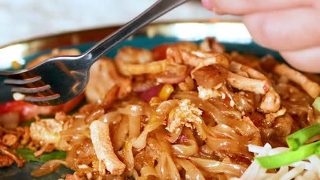 a detailed view of shrimp pad thai being enjoyed with a fork and spoon, highlighting the vibrant ingredients.