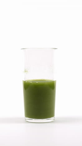 la mano agitando un batido verde con un tenedor en un vaso transparente contra un fondo blanco