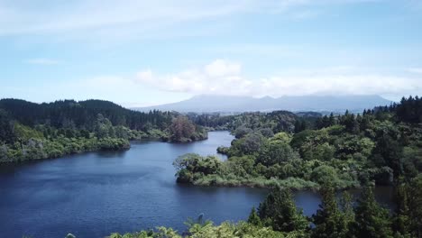 drone shot, rising over trees towards lake with mount taranaki at the back, in new plymouth, new zealand