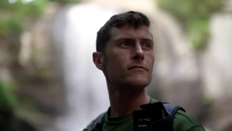 young attractive man looking around in reflection at nature and waterfall behind him, environmental, hiking, contemplation, discovery