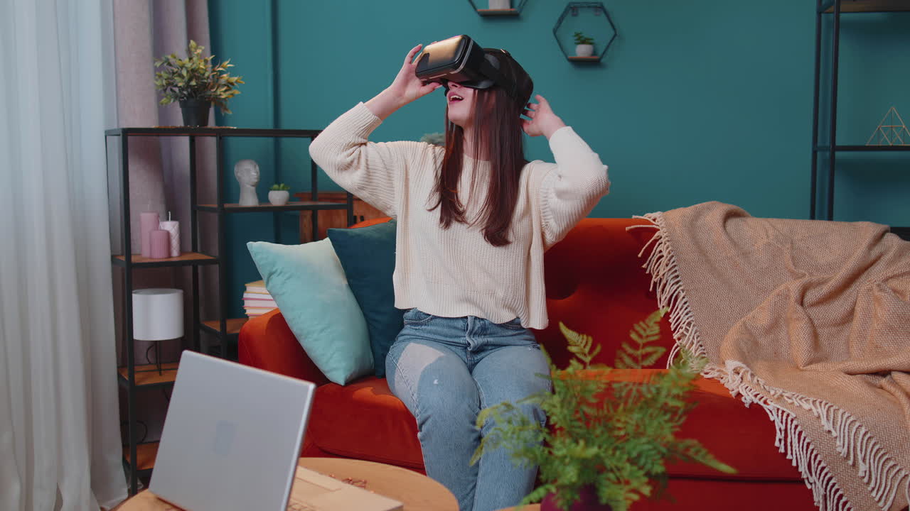 una mujer joven usa gafas de realidad virtual en casa, disfrutando del concepto de video moviendo las manos en el aire